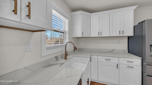 kitchen featuring white cabinets, a sink, stainless steel refrigerator with ice dispenser, and light stone countertops