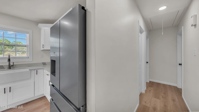 kitchen featuring white cabinets, light countertops, light wood-style floors, stainless steel refrigerator with ice dispenser, and a sink