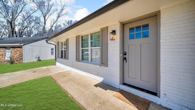 view of exterior entry with brick siding and a lawn