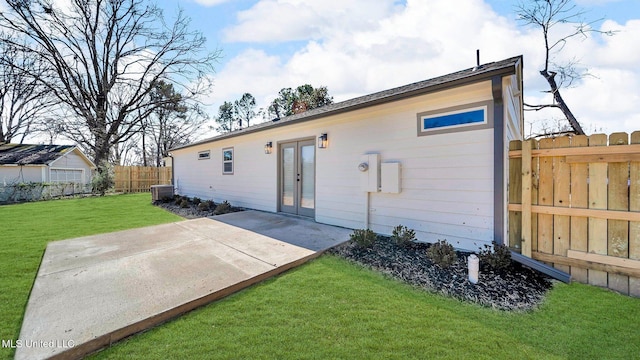 rear view of property featuring a patio, central AC, fence, french doors, and a lawn