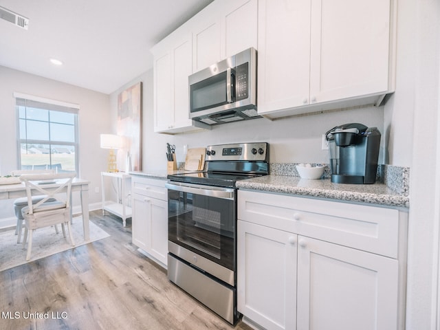 kitchen with stainless steel appliances, visible vents, light wood-style floors, white cabinets, and light stone countertops