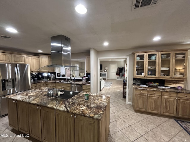 kitchen with a center island with sink, light tile patterned floors, dark stone countertops, island exhaust hood, and stainless steel appliances