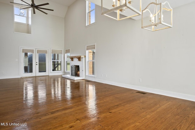 unfurnished living room with plenty of natural light, ceiling fan with notable chandelier, a high ceiling, and a brick fireplace