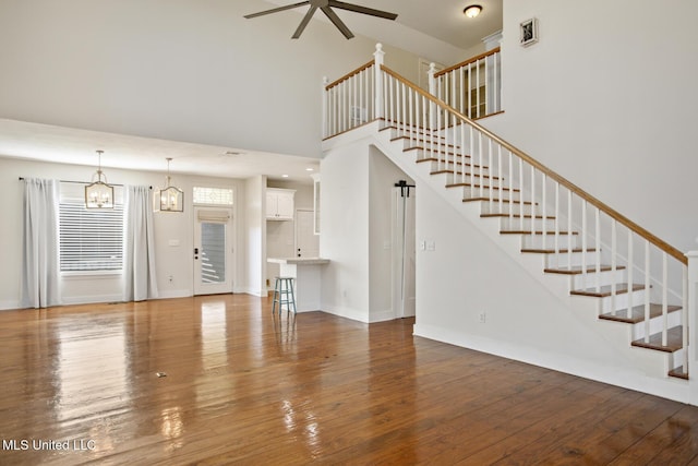 unfurnished living room with ceiling fan with notable chandelier, dark hardwood / wood-style flooring, and a high ceiling