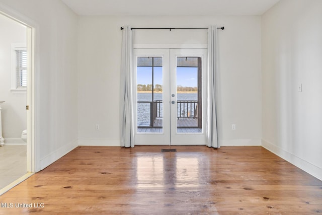 spare room with french doors, a water view, and light hardwood / wood-style flooring