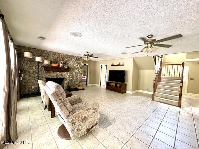 living room featuring a textured ceiling, a ceiling fan, stairs, and light tile patterned flooring