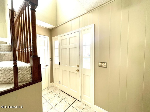 entryway featuring light tile patterned floors, baseboards, stairs, and lofted ceiling