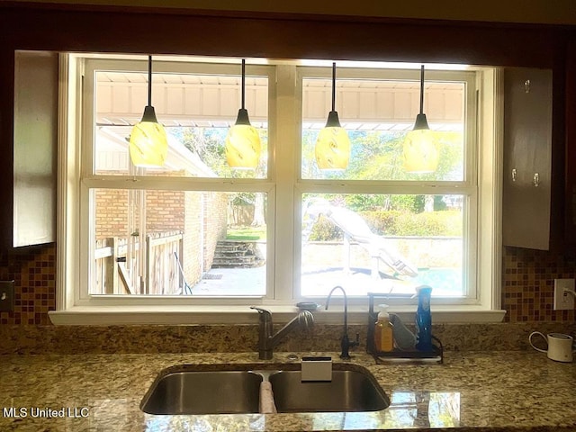 room details featuring a sink, decorative backsplash, stone countertops, and decorative light fixtures