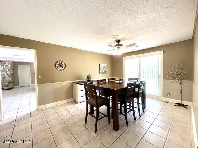 dining space featuring a textured ceiling, ceiling fan, wainscoting, and light tile patterned floors
