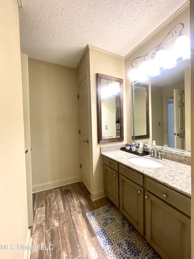 bathroom with baseboards, a textured ceiling, wood finished floors, and vanity