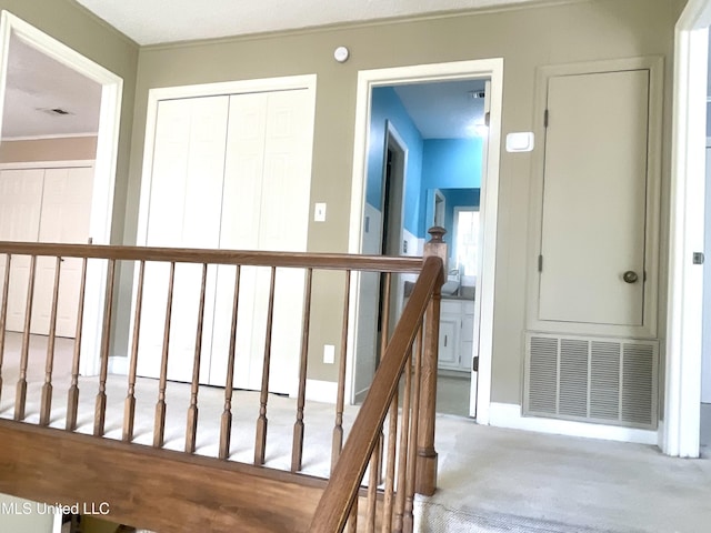 corridor featuring visible vents, ornamental molding, carpet floors, and an upstairs landing