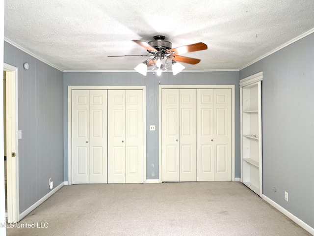 unfurnished bedroom with carpet floors, baseboards, crown molding, and two closets