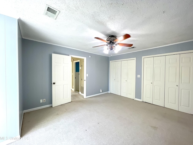 unfurnished bedroom featuring crown molding, multiple closets, carpet, baseboards, and visible vents