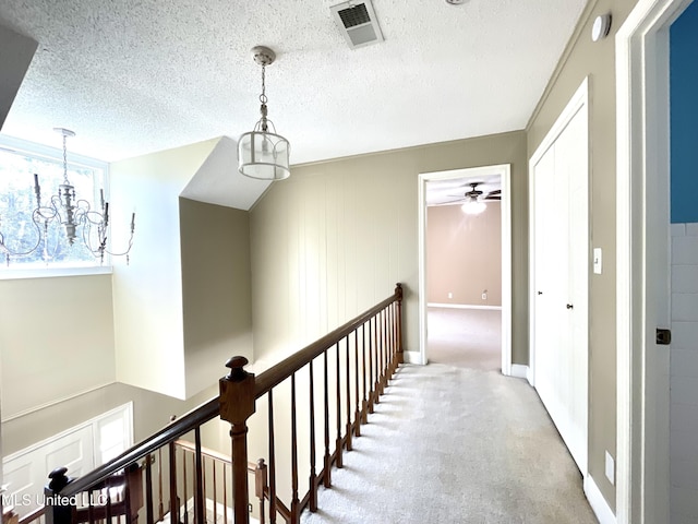 corridor featuring visible vents, baseboards, a textured ceiling, a chandelier, and carpet flooring