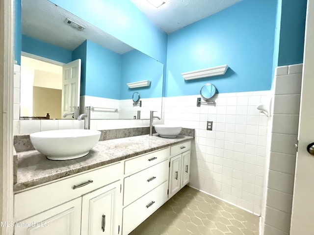 bathroom featuring double vanity, a sink, wainscoting, and tile walls