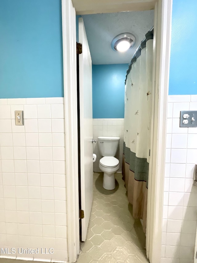 bathroom with toilet, tile walls, tile patterned flooring, and a wainscoted wall