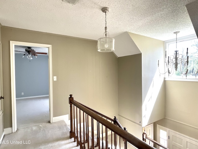 corridor featuring an inviting chandelier, carpet floors, a textured ceiling, baseboards, and an upstairs landing
