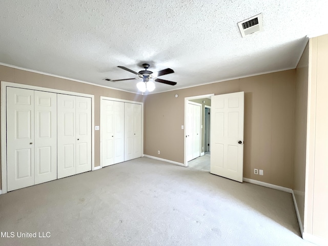 unfurnished bedroom with baseboards, visible vents, two closets, and light colored carpet