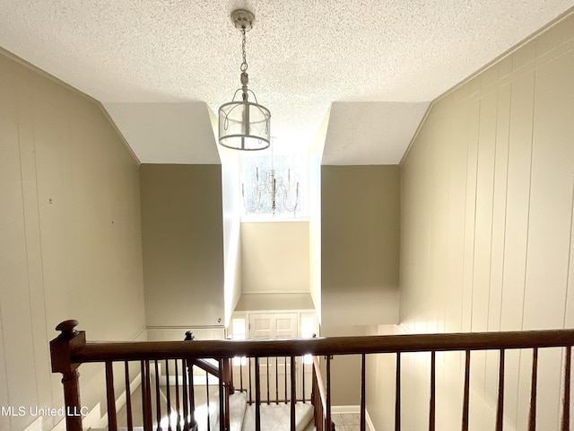 stairway with an inviting chandelier, a decorative wall, and a textured ceiling