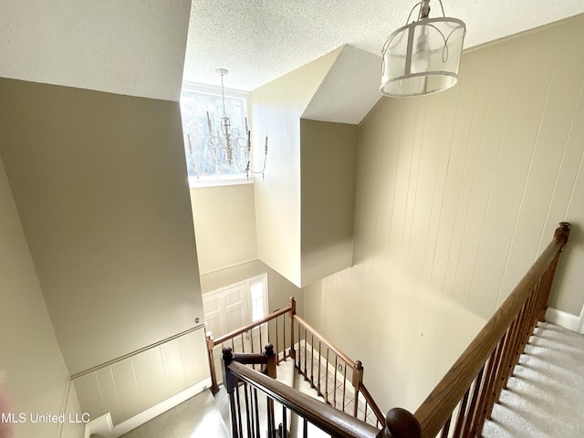 stairway with an inviting chandelier and a textured ceiling