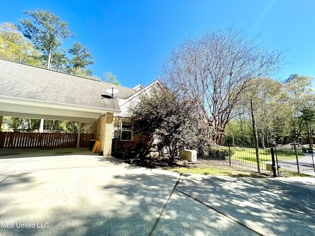 view of side of property with brick siding, a gate, fence, and concrete driveway