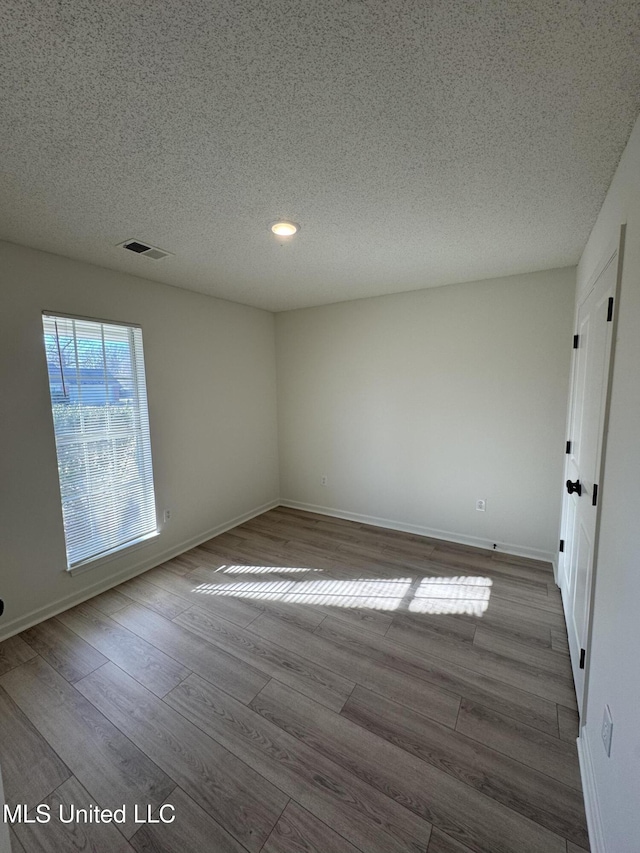 empty room featuring a textured ceiling, wood finished floors, visible vents, and baseboards