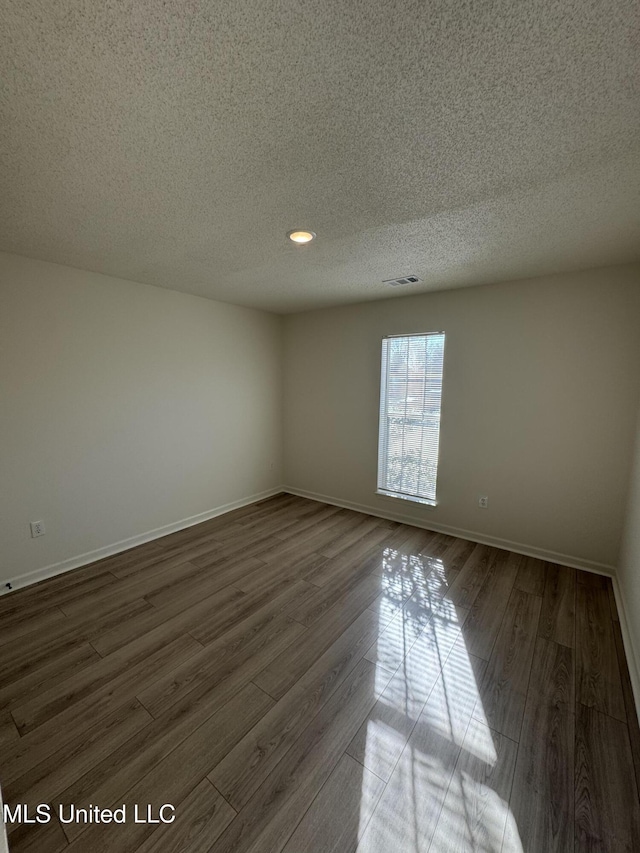 spare room featuring visible vents, baseboards, a textured ceiling, and dark wood-style floors