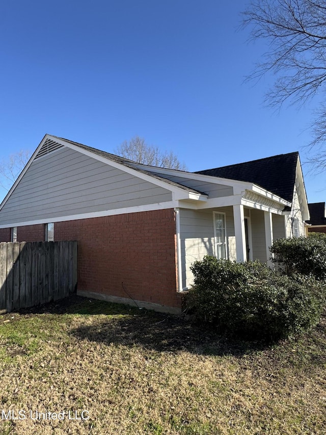 view of home's exterior featuring brick siding, a lawn, and fence