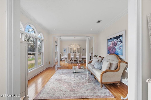 living room with light hardwood / wood-style floors, ornamental molding, a wealth of natural light, and an inviting chandelier