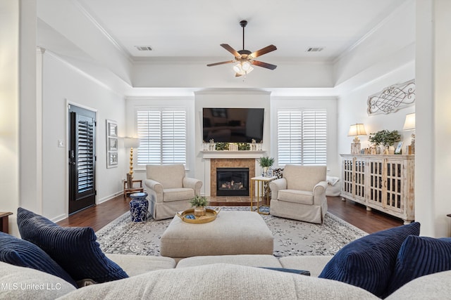 living room with a tray ceiling, crown molding, dark wood-type flooring, and ceiling fan