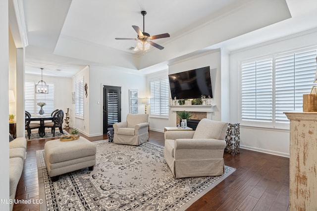 living room with ceiling fan with notable chandelier, dark wood-type flooring, ornamental molding, and a raised ceiling