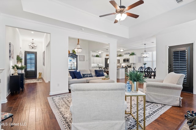 living room featuring a tray ceiling, dark wood-type flooring, ornamental molding, and ceiling fan with notable chandelier