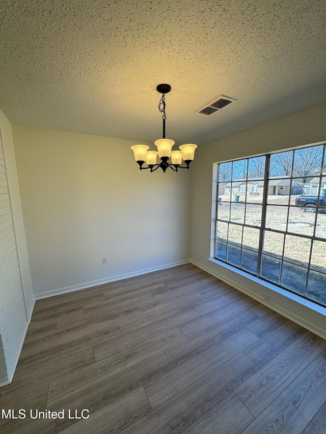 spare room featuring baseboards, visible vents, dark wood finished floors, an inviting chandelier, and a textured ceiling