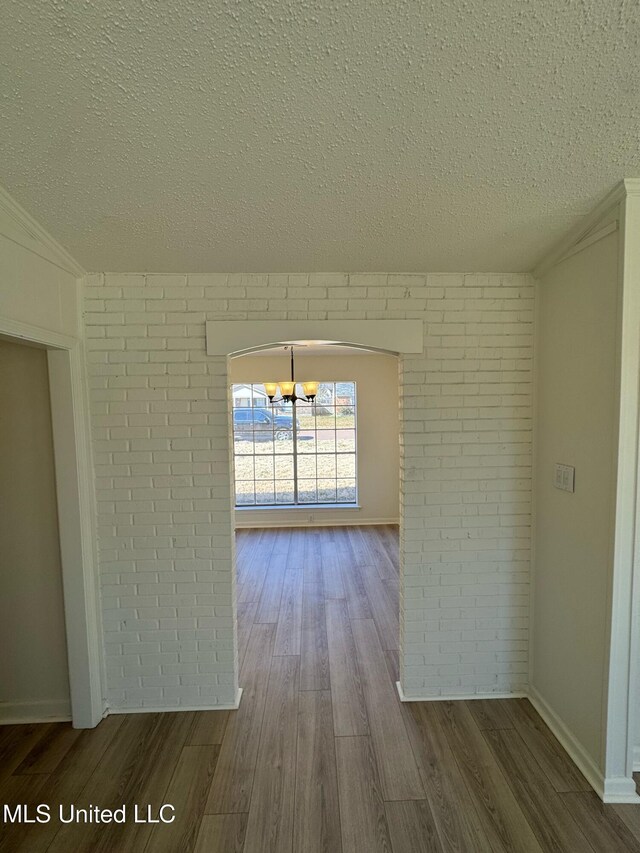 unfurnished room featuring a textured ceiling, brick wall, and wood finished floors