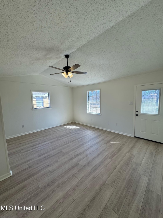 spare room with baseboards, lofted ceiling, ceiling fan, wood finished floors, and a textured ceiling