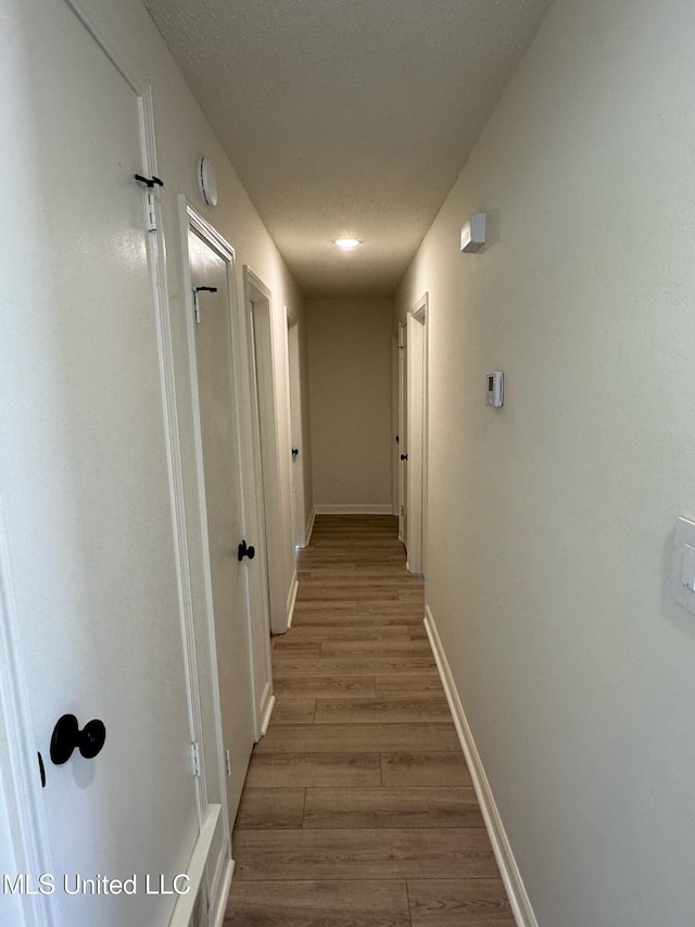 hallway with a textured ceiling, baseboards, and wood finished floors