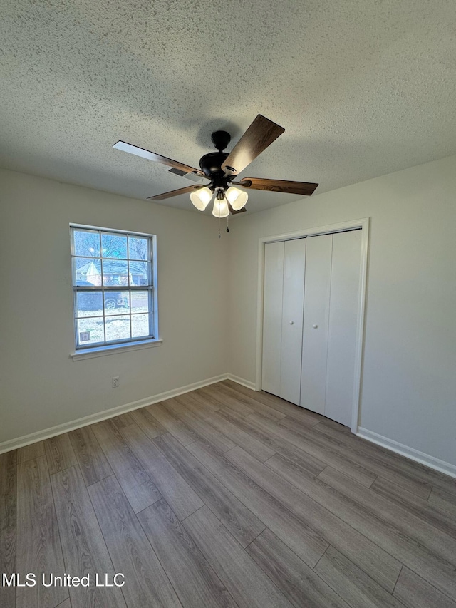 unfurnished bedroom featuring a closet, a ceiling fan, a textured ceiling, wood finished floors, and baseboards