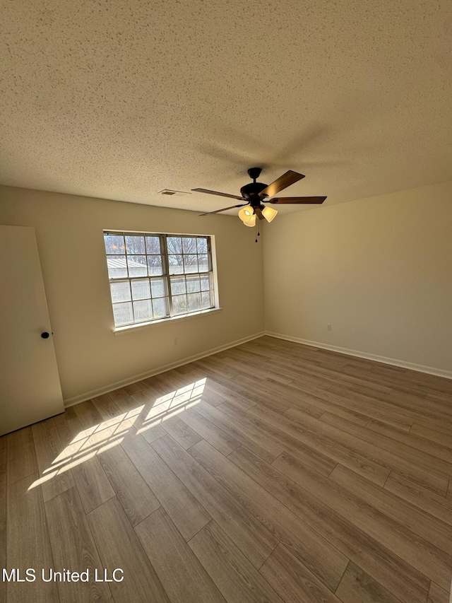 spare room with ceiling fan, a textured ceiling, baseboards, and wood finished floors