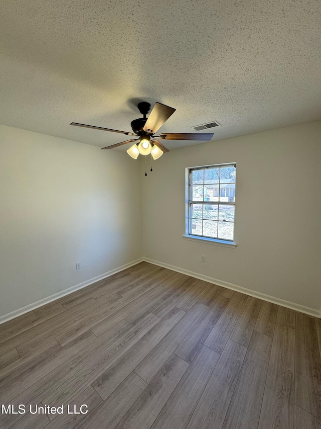 empty room with a textured ceiling, ceiling fan, wood finished floors, visible vents, and baseboards