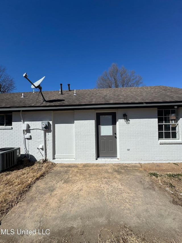 rear view of house featuring central AC unit, a shingled roof, and brick siding