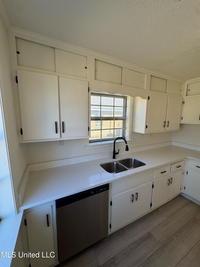 kitchen with wood finished floors, light countertops, a textured ceiling, stainless steel dishwasher, and a sink