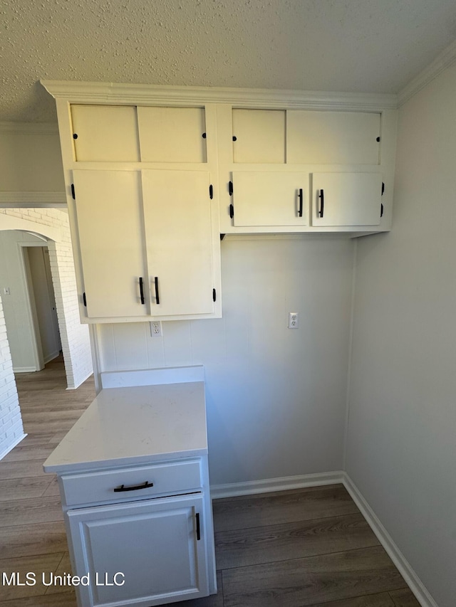 clothes washing area featuring baseboards, arched walkways, wood finished floors, a textured ceiling, and crown molding