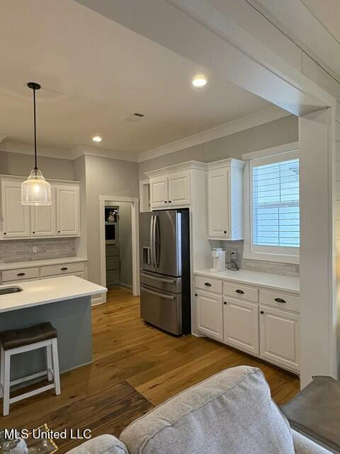 kitchen featuring stainless steel refrigerator with ice dispenser, tasteful backsplash, hardwood / wood-style flooring, pendant lighting, and white cabinets