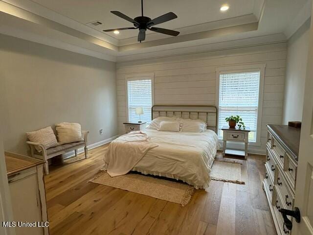 bedroom with crown molding, a tray ceiling, light hardwood / wood-style floors, and ceiling fan