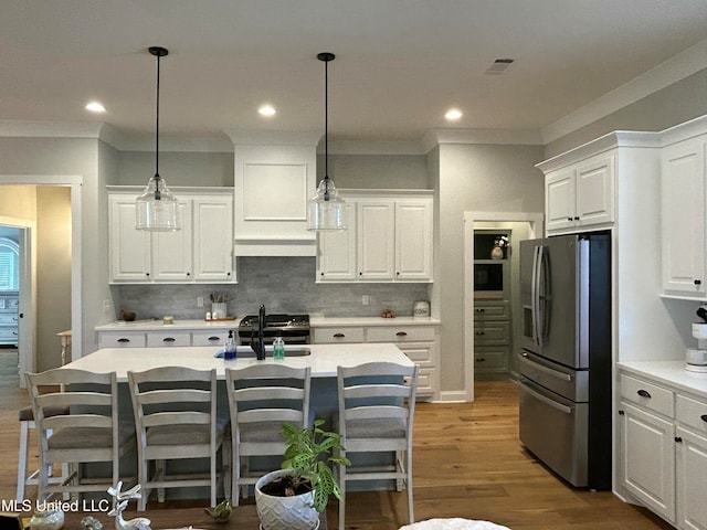 kitchen with white cabinetry, backsplash, a center island with sink, stainless steel fridge with ice dispenser, and decorative light fixtures