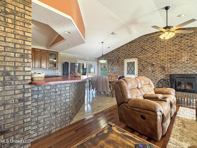 living room featuring brick wall, a textured ceiling, lofted ceiling, dark hardwood / wood-style flooring, and ceiling fan