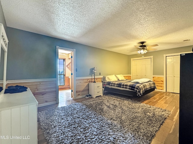 bedroom featuring ceiling fan, two closets, a textured ceiling, and hardwood / wood-style floors