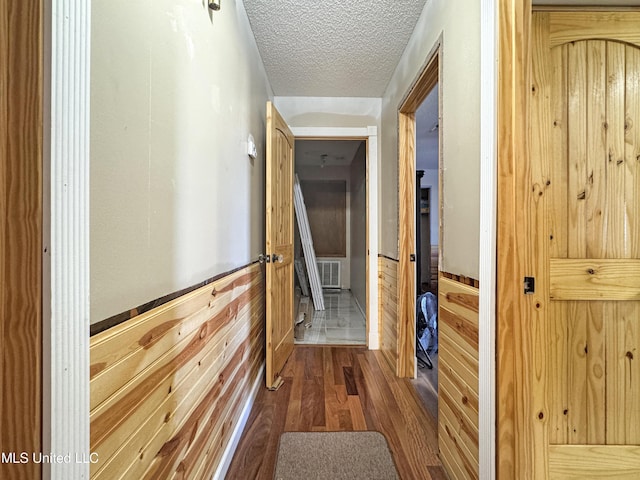 corridor with wood walls, hardwood / wood-style floors, and a textured ceiling