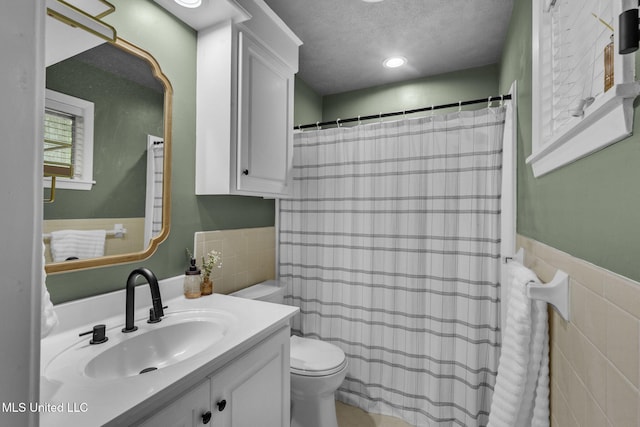 bathroom featuring a textured ceiling, tile walls, wainscoting, vanity, and toilet