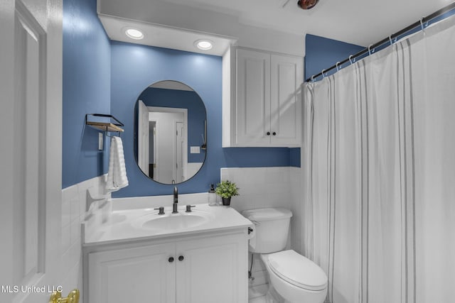 bathroom with tile walls, a wainscoted wall, vanity, toilet, and recessed lighting